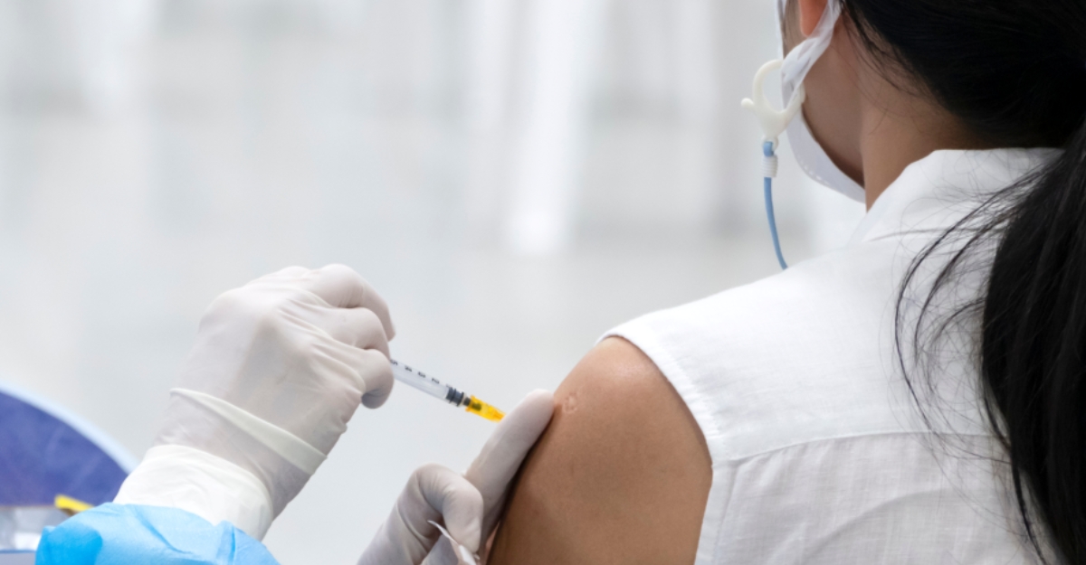 Doctor giving vaccine booster dose to woman patient wearing protective face mask.